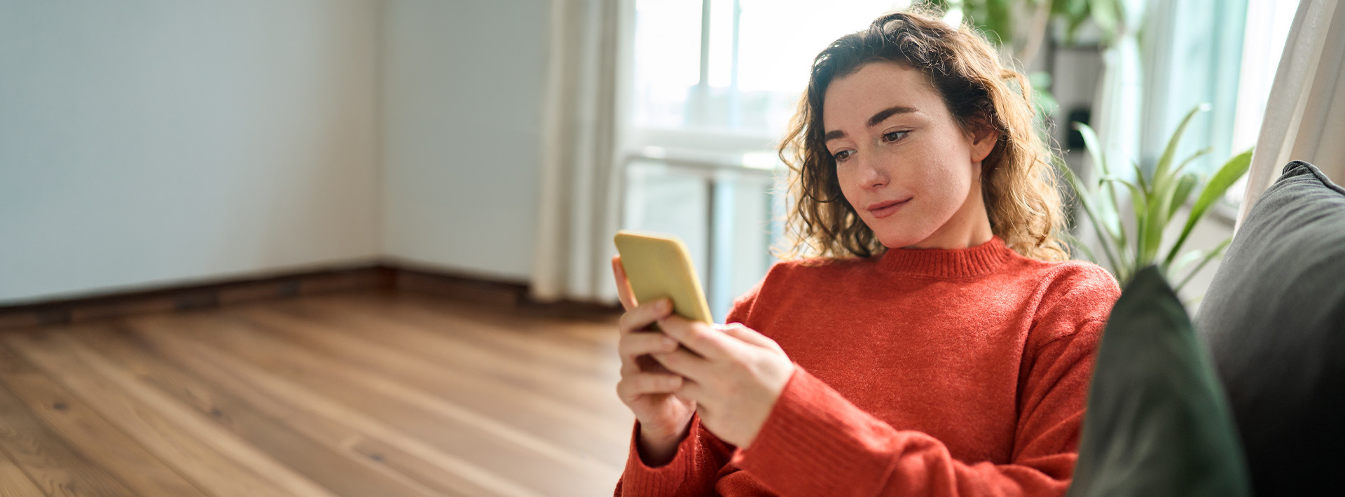 Kobieta siedzi na kanapie, korzysta ze smartfona, składając wniosek o kredyt gotówkowy w aplikacji mobilnej