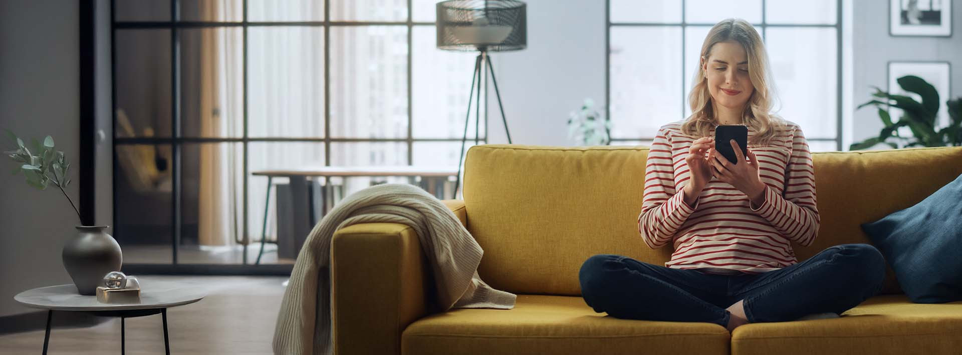 Kobieta siedzi na kanapie i sprawdza informacje w telefonie.