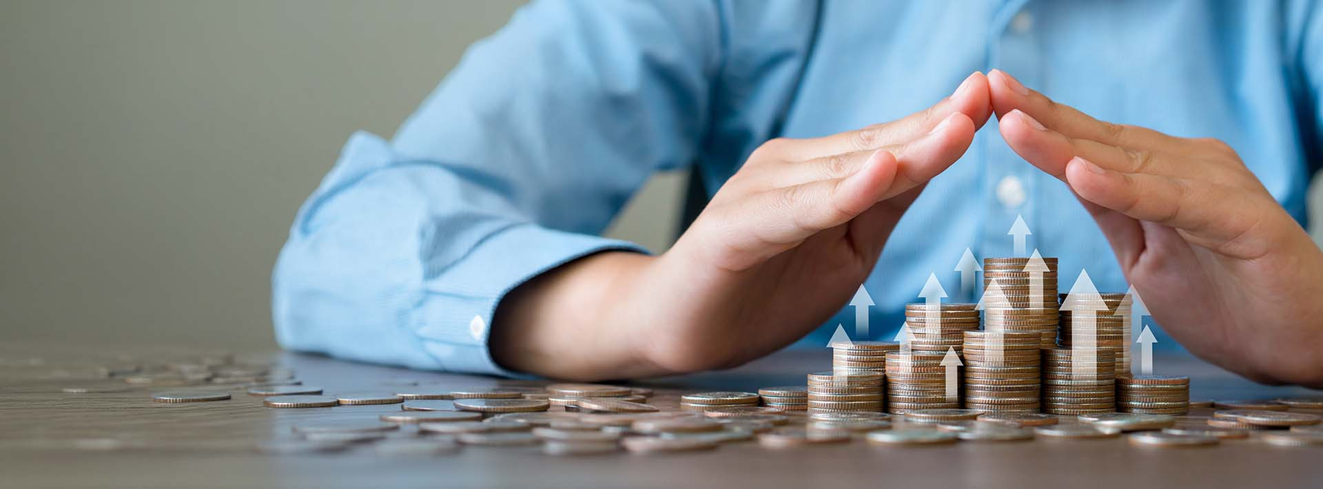 Dłonie tworzą kształt ochronny nad rosnącymi stosami monet; strzałki w górę wskazują wzrost wartości oszczędności lub inwestycji