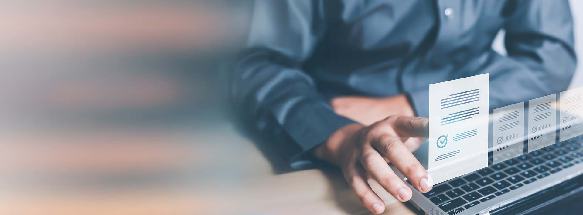 Dłoń wskazująca na dokument przy laptopie