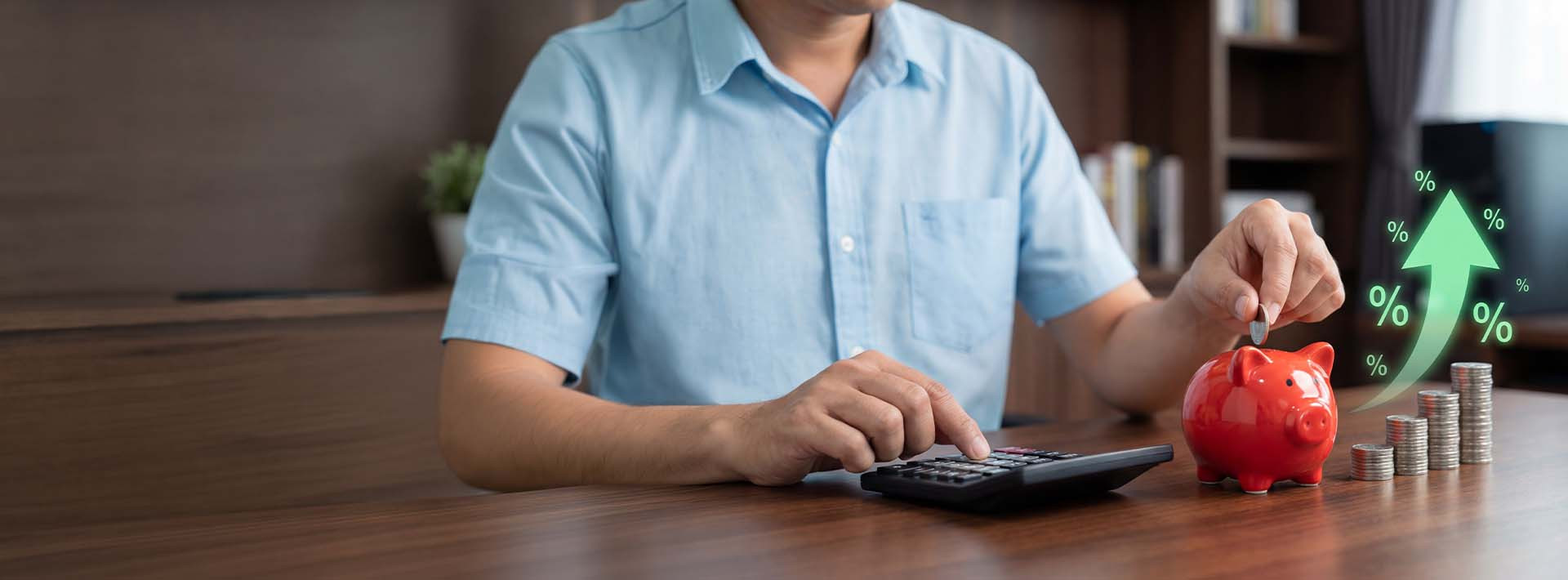Mężczyzna odkłada monetę do czerwonej skarbonki obok kalkulatora i stosów monet; grafika ze strzałką w górę i symbolami procentów sugeruje wzrost oszczędności lub zysków