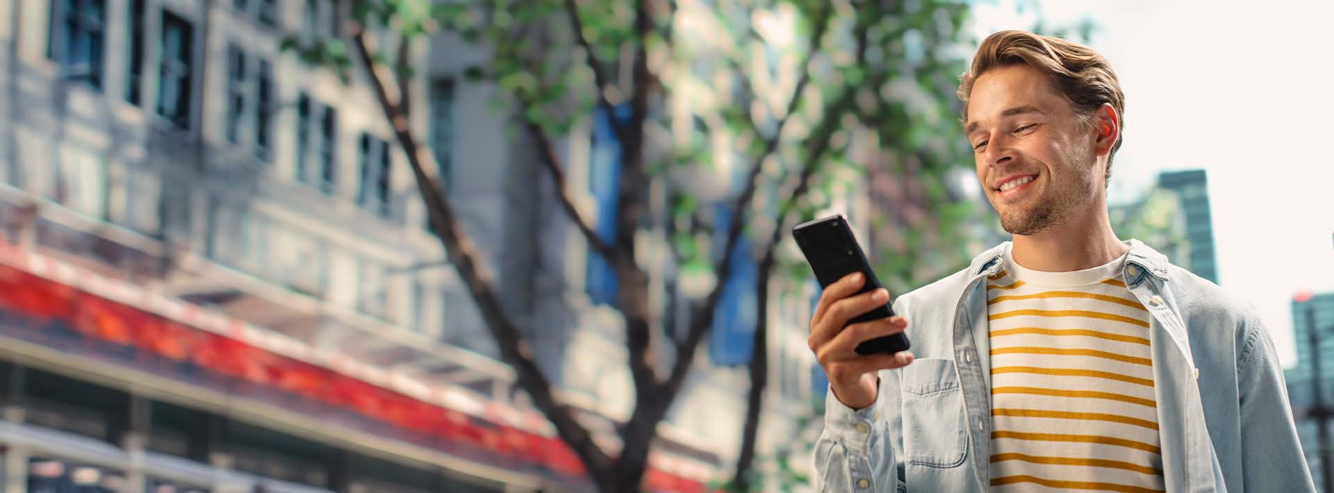 Osoba korzystająca ze smartfona w przestrzeni miejskiej, ilustrująca sprawdzanie terminu zakończenia lokaty i zarządzanie oszczędnościami w bankowości online.