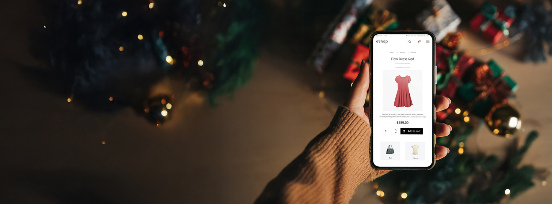 na grafice widzimy dłoń na tle prezentów, trzymającą telefon, na którym widać screena ze sklepu online