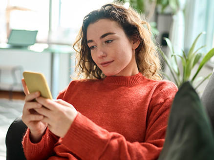 Kobieta siedzi na kanapie, korzysta ze smartfona, składając wniosek o kredyt gotówkowy w aplikacji mobilnej
