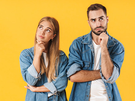 Kobieta i mężczyzna w dżinsowych koszulach wykonujący gest zadumy, patrzą w górę, co sugeruje zastanawianie się i niepewność