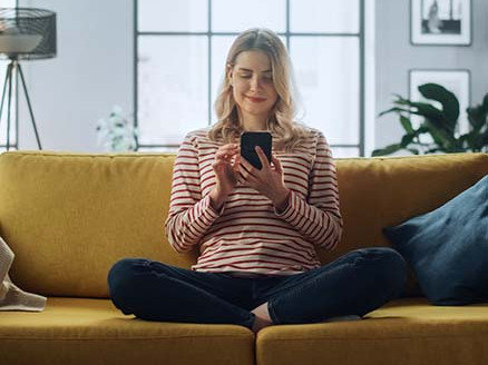 Kobieta siedzi na kanapie i sprawdza informacje w telefonie.