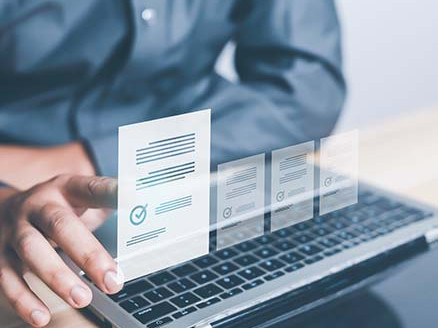 Dłoń wskazująca na dokument przy laptopie