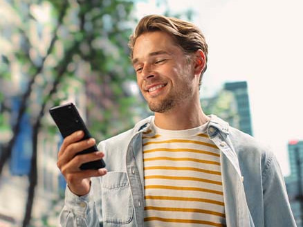 Osoba korzystająca ze smartfona w przestrzeni miejskiej, ilustrująca sprawdzanie terminu zakończenia lokaty i zarządzanie oszczędnościami w bankowości online.