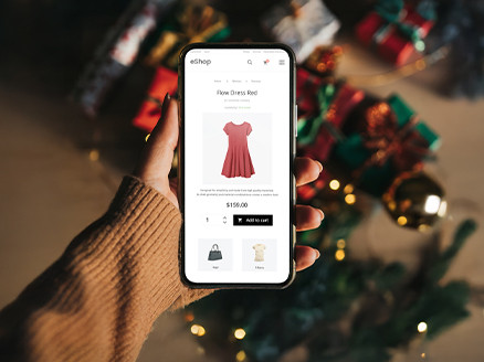 na grafice widzimy dłoń na tle prezentów, trzymającą telefon, na którym widać screena ze sklepu online