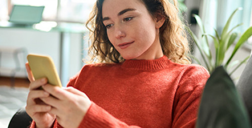 Kobieta siedzi na kanapie, korzysta ze smartfona, składając wniosek o kredyt gotówkowy w aplikacji mobilnej
