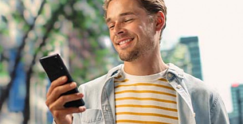 Osoba korzystająca ze smartfona w przestrzeni miejskiej, ilustrująca sprawdzanie terminu zakończenia lokaty i zarządzanie oszczędnościami w bankowości online.