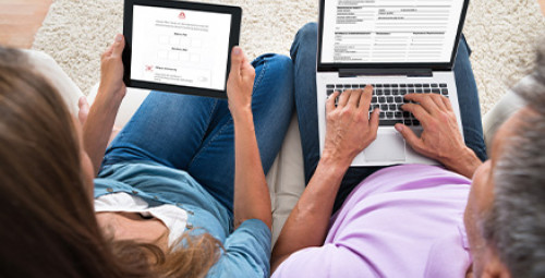 zdjęcie przedstawia dwie osoby siedzące na kanapie, jedna trzyma laptopa, a druga tablet